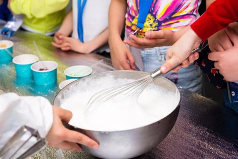 bambini mescolano un liquido schiumoso in una ciotola di metallo usando una frusta durante un divertente esperimento scientifico di cucina pratica per fare il gelato.